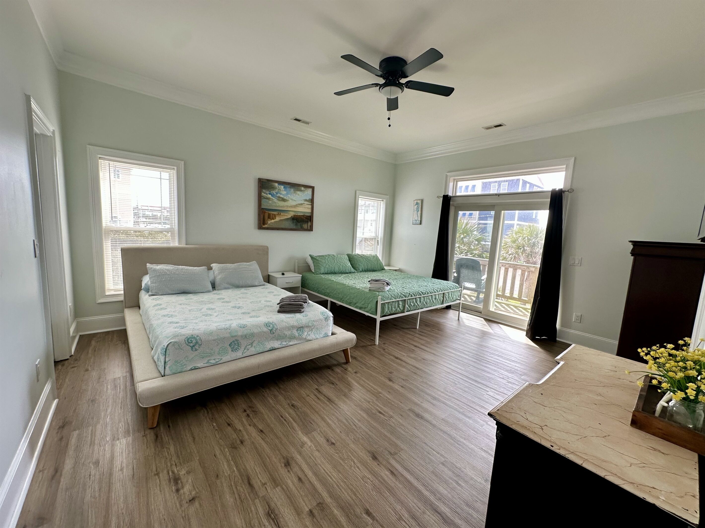 A bedroom with two beds, a ceiling fan, and a balcony with a view.