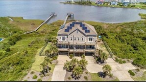 A large two-story house with a balcony, surrounded by a well-maintained lawn and a dock extending into a body of water. - “Coastal Haven” Gorgeous 6 bedroom home pool (North Topsail Beach)