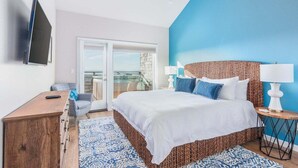Un dormitorio con una cama grande, televisión, cómoda de madera y balcón con puerta de cristal.