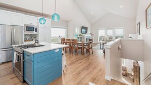 Una cocina moderna con una isla azul, electrodomésticos de acero inoxidable y un comedor con sillas de madera.