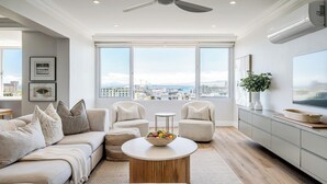 Een moderne woonkamer met een bank, fauteuils, een salontafel en uitzicht op de stad door grote ramen.