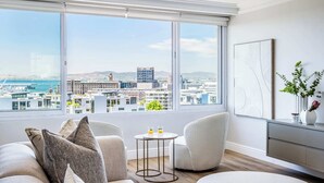 Een moderne woonkamer met een groot raam dat uitzicht geeft op de stad, comfortabele zitplaatsen en een minimalistische inrichting.
