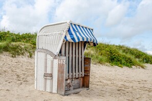 A beach hut with a striped awning, a number '462' on the side, and a wooden door.