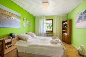 Une chambre à coucher avec un lit, une table de chevet, une commode en bois et une fenêtre avec des rideaux.