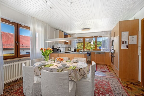Une cuisine moderne avec des meubles en bois, un coin repas avec une table dressée pour quatre personnes, et une vue sur l’extérieur.