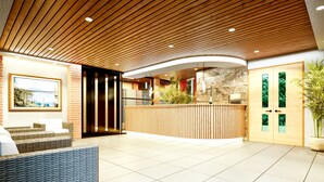A reception area with a wooden ceiling, a reception desk, a stone wall, and a large window. - Bella Ella Hotel (Kasoa)
