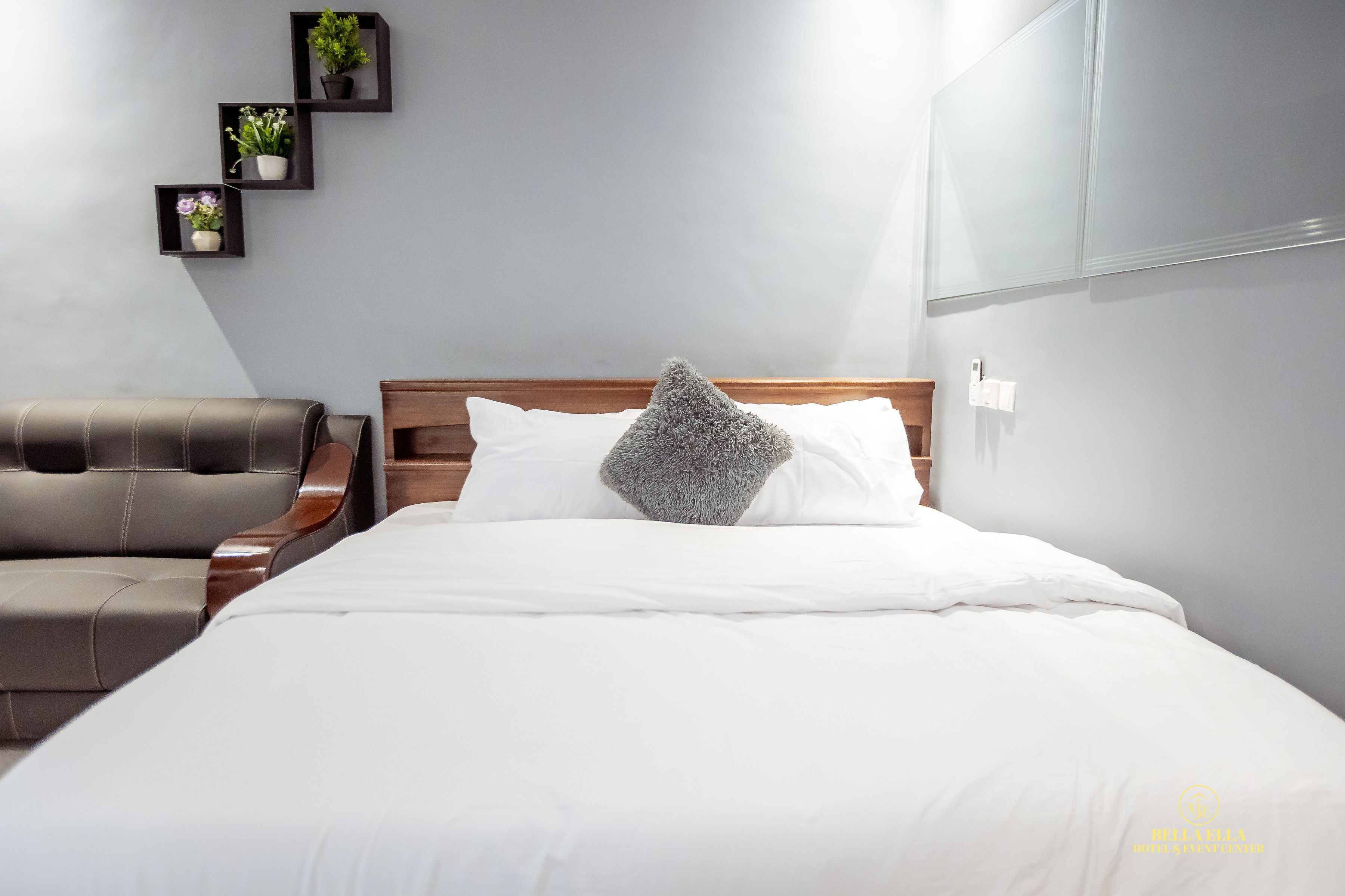 A neatly arranged bedroom with a bed, a wooden headboard, a grey furry throw pillow, and a brown leather chair.