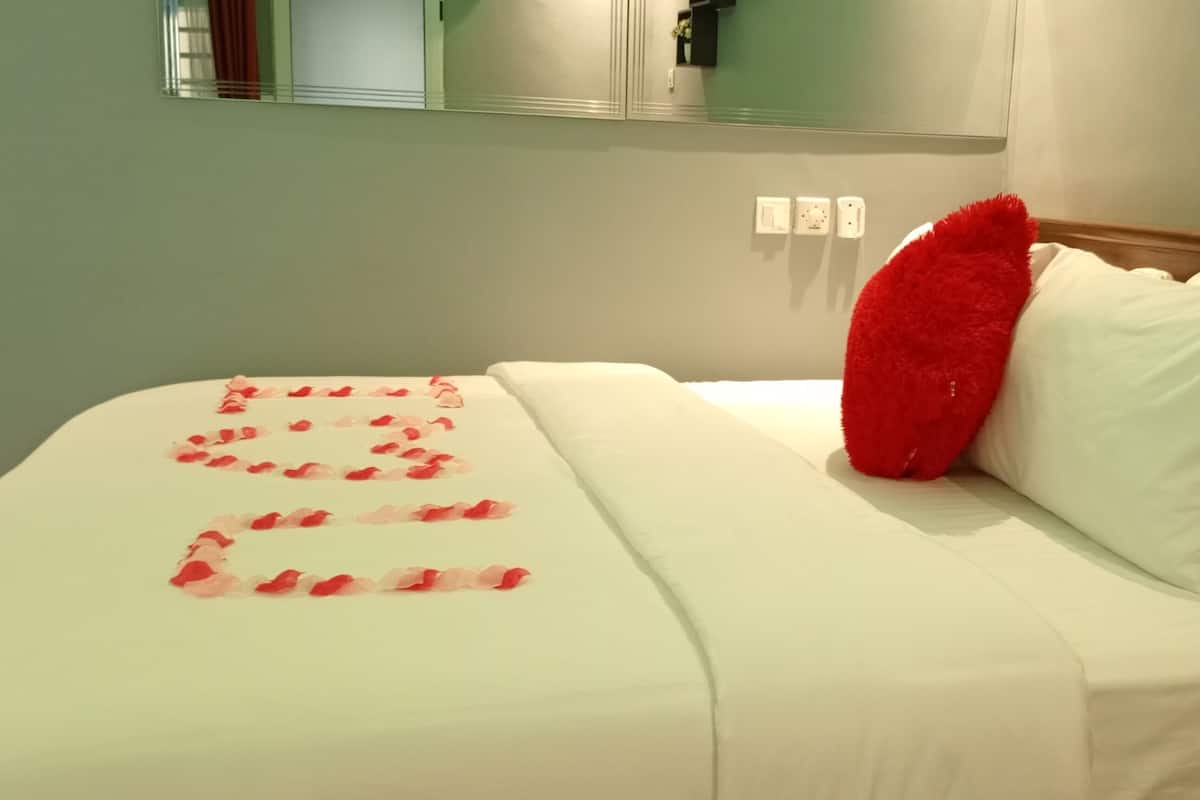 Ein Hotelzimmer mit einem Bett, einem roten Kissen und Rosenblättern, die auf dem Bett drapiert sind.