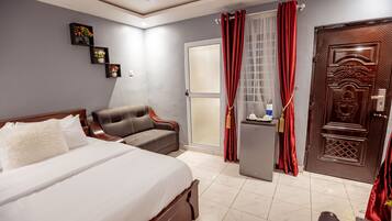 A hotel room with a bed, a sofa, a desk, and a door.