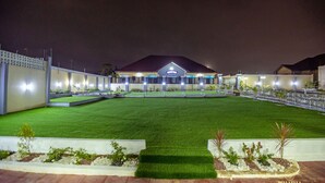 A hotel with a well-maintained lawn, a central building with a sign, and a gated entrance. - Bella Ella Hotel (Kasoa)