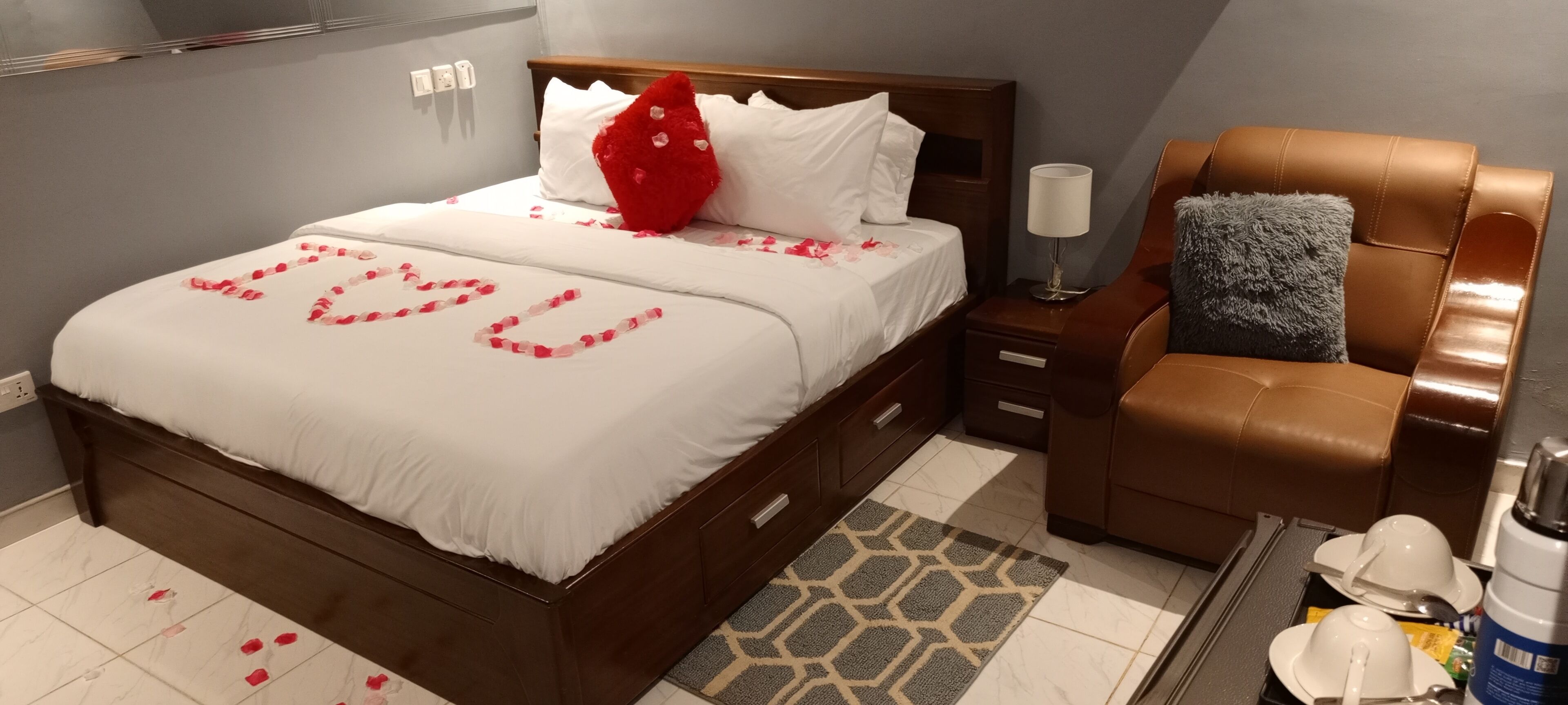 A neatly made bed with a white comforter and a red heart-shaped decoration.