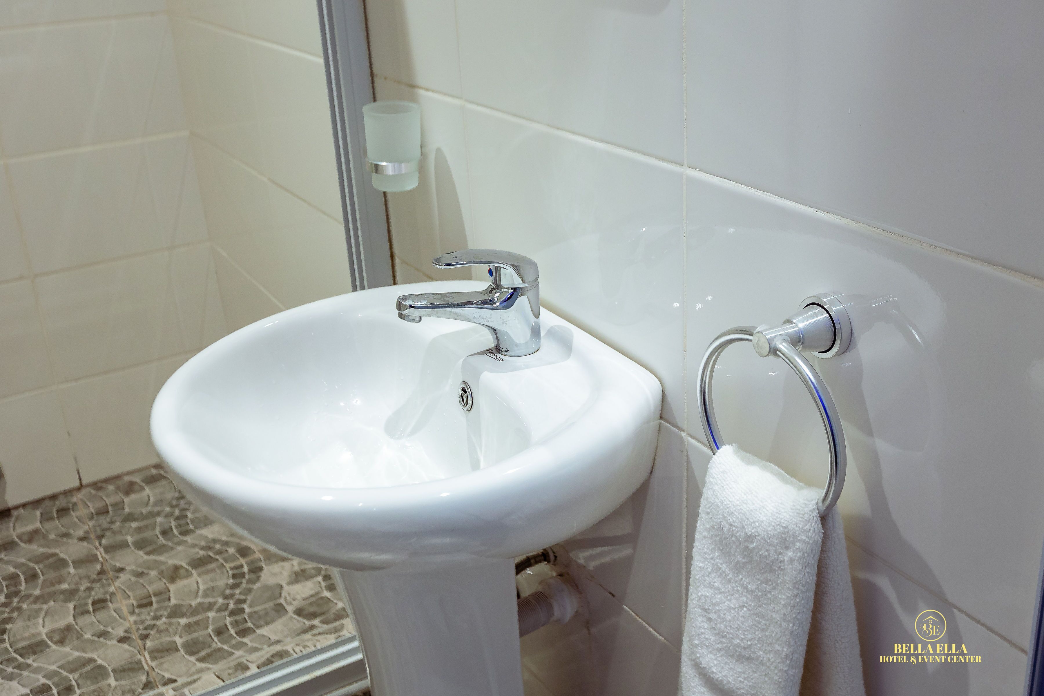 Un baño con un lavamanos blanco, un dispensador de jabón de vidrio y un perchero para toallas.