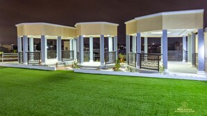 A hotel with three illuminated pavilions connected by a central walkway, surrounded by well-maintained grass. - Bella Ella Hotel (Kasoa)