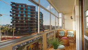 A balcony with wicker furniture, a potted plant, and a view of a modern building. - GuestReady - Varanda de belas lembranças (Funchal)