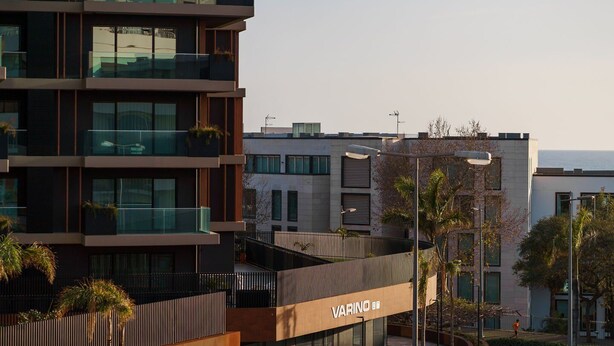 A modern building with multiple balconies, a visible sign reading "VARINO," and a clear view of the sea in the background. - GuestReady - Varanda de belas lembranças (Funchal)