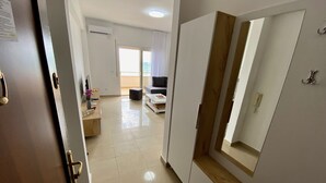 Corredor que leva a uma sala de estar com sofá, televisão e janela com cortinas.