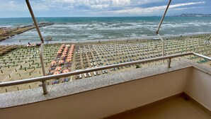 Uma praia com fileiras de guarda-sóis e espreguiçadeiras, um corrimão e vista para o oceano.