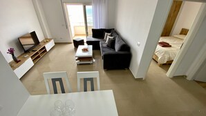 Uma sala de estar moderna com um sofá, uma mesa de centro e uma televisão. Há uma mesa de jantar com cadeiras em primeiro plano.