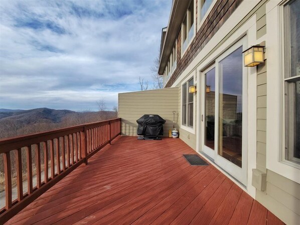 A wooden deck with a grill and outdoor lighting, overlooking a mountainous landscape.