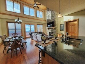 A spacious kitchen with a stone fireplace, a dining area with wooden chairs, and a large window overlooking a scenic view.