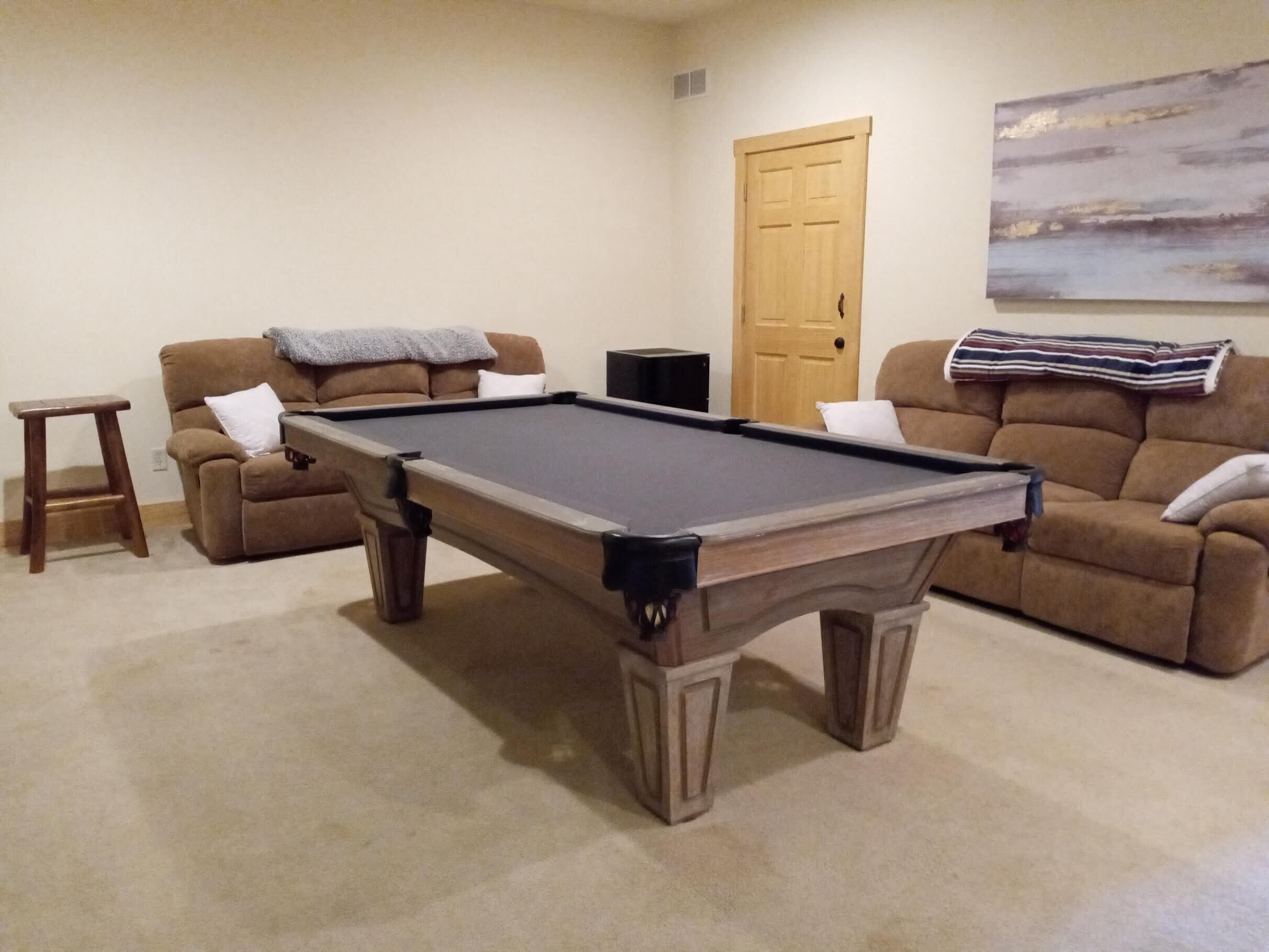 A pool table in a living room with a sofa and a door in the background.