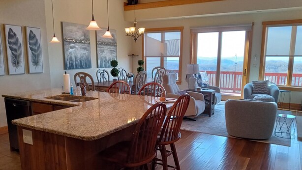A spacious kitchen with a large island, wooden chairs, a dining table, and a view of the mountains through large windows. - New! Peaceful Mountain Views, Deck, Trails nearby, Pool Table. (Mars Hill)