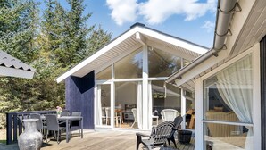 A wooden deck with outdoor furniture, a glass-enclosed room, and a view of the surrounding trees.