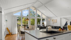 A modern kitchen with white cabinetry, a large island with a sink, and a dining area with chairs.