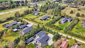 An aerial view of a residential area with multiple houses, surrounded by greenery and fields.
