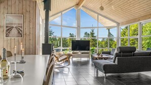 A modern living room with a large TV, wooden ceiling, and large windows offering a view of trees. - "Nayati" - 2km from the sea by Interhome (Saltum)