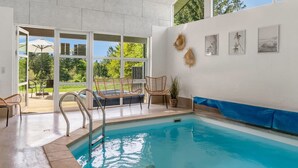 A modern indoor pool area with clear glass walls, a pool, and a patio with outdoor furniture. - "Nayati" - 2km from the sea by Interhome (Saltum)