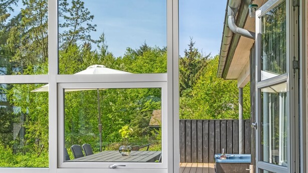 A modern outdoor seating area with a glass enclosure, a wooden deck, and a view of a lush garden. - "Nayati" - 2km from the sea by Interhome (Saltum)