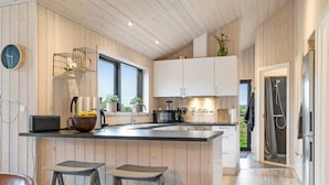 Une cuisine moderne avec un lambris en bois, un grand îlot central doté de tabourets, une fenêtre et une vue sur la verdure à l’extérieur.