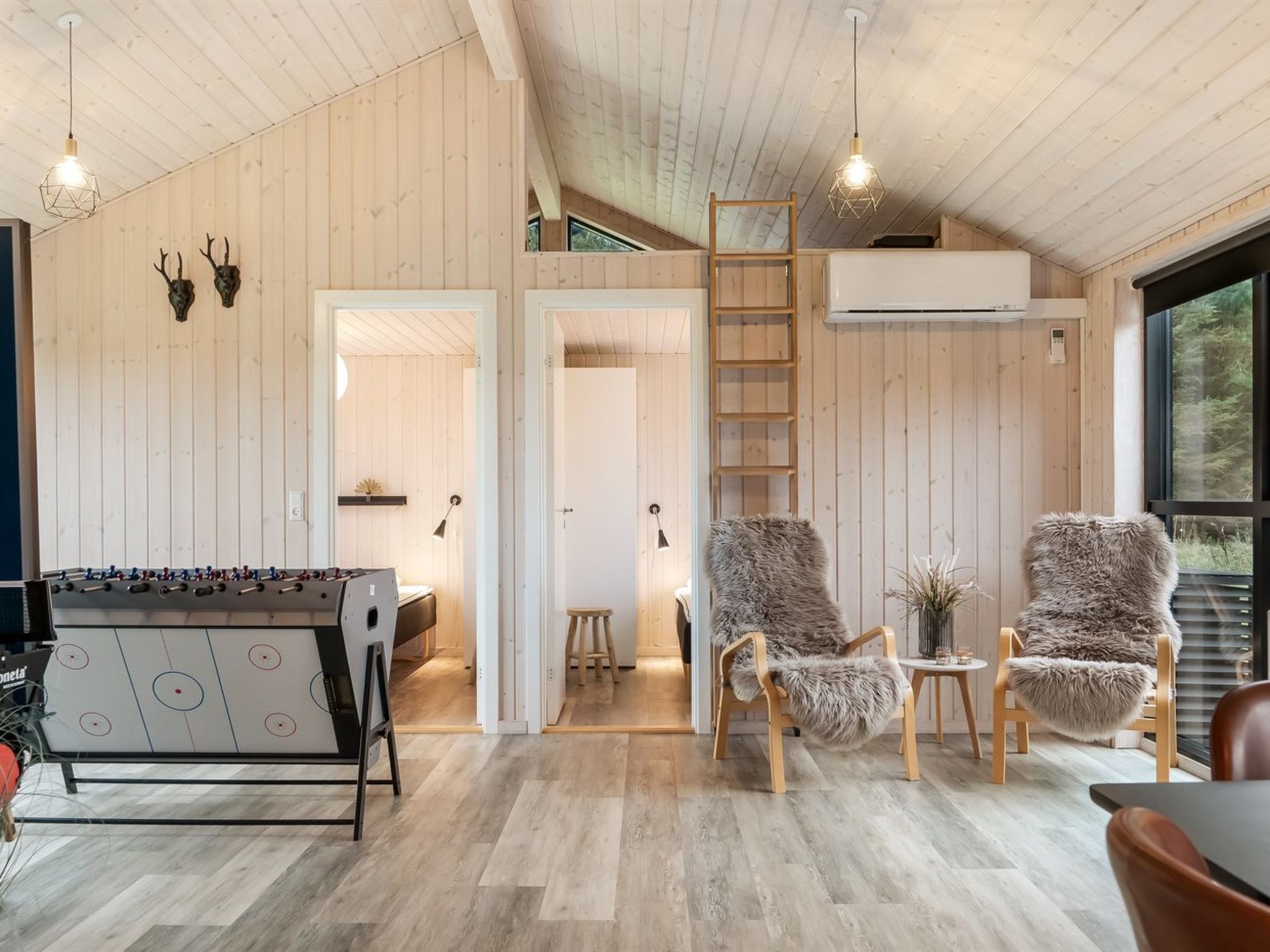 A cozy room with wooden walls, a foosball table, two furry chairs, and a ladder leading to a loft.