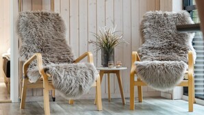 Une pièce avec deux fauteuils recouverts de fausse fourrure, une petite table sur laquelle est posé un vase de fleurs et un mur en bois.