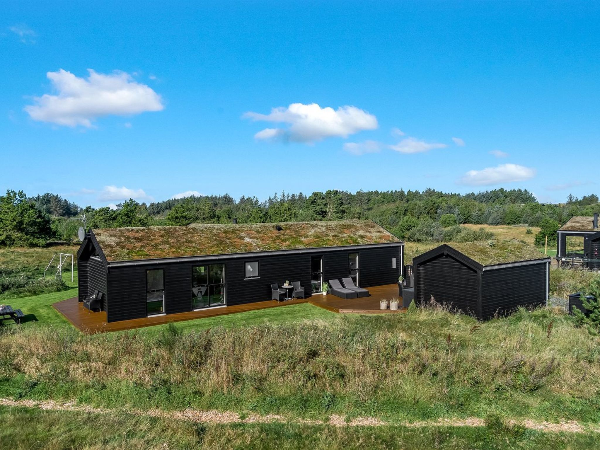 Um edifício moderno, de cor preta, com um telhado verde, rodeado por um campo relvado e árvores.
