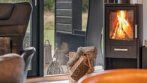 Une pièce chaleureuse avec une cheminée, un panier en osier rempli de bois de chauffage et un fauteuil.