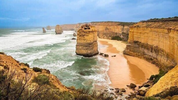 A coastal landscape with prominent rock formations and a sandy beach.