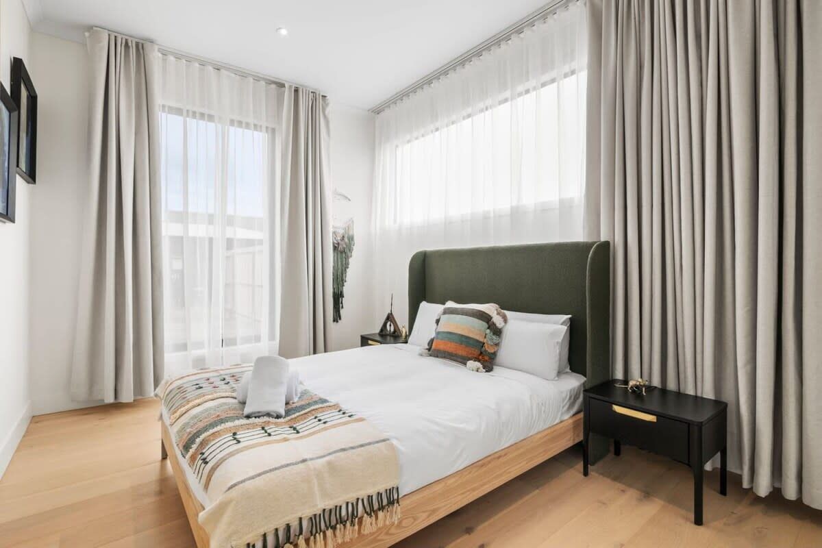 A modern bedroom with a large bed, a bedside table, and a view of the outdoors through sheer curtains.