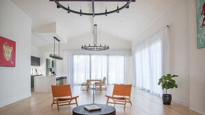 A spacious living area with a round coffee table, two wooden chairs, a chandelier, and a potted plant.
