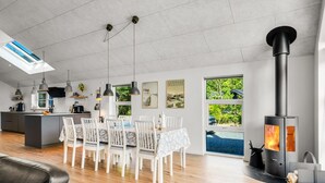 Una cocina moderna con una isla central, luces colgantes y un comedor con mesa y sillas blancas.