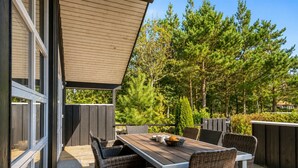 Un patio al aire libre con una mesa y sillas, rodeado de un deck de madera y árboles.