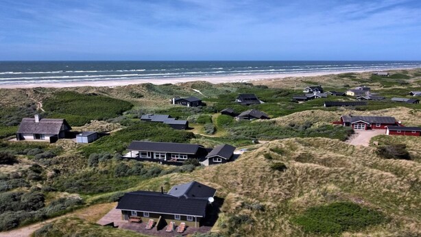 Vue aérienne d’une zone côtière avec de nombreuses maisons entourées de dunes et de végétation.