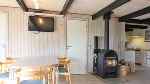 Un intérieur en bois avec une table ronde et des chaises, un téléviseur fixé au mur et un poêle à bois.