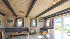 L’intérieur chaleureux d’un chalet avec un plafond en bois, un canapé, une table à manger et une vue magnifique à travers de grandes fenêtres.