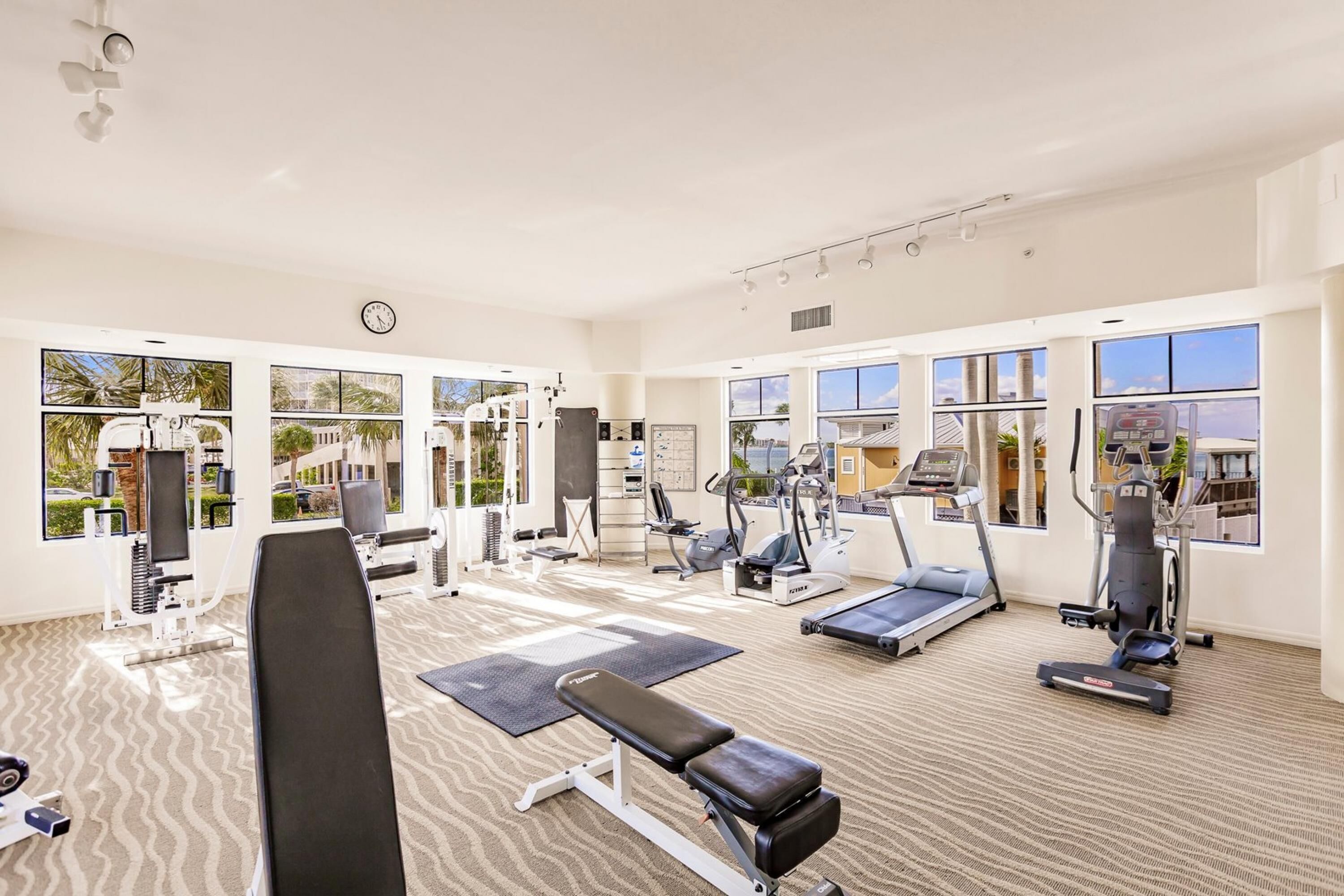 A spacious gym with various exercise equipment, large windows, and a clean, modern design.