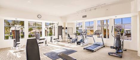 A spacious gym with various exercise equipment, large windows, and a clean, modern design.