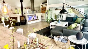 Una sala de estar moderna con televisor, sofá y mesa de centro. Hay una chimenea, un área de cocina y una escalera que conduce a otro nivel.