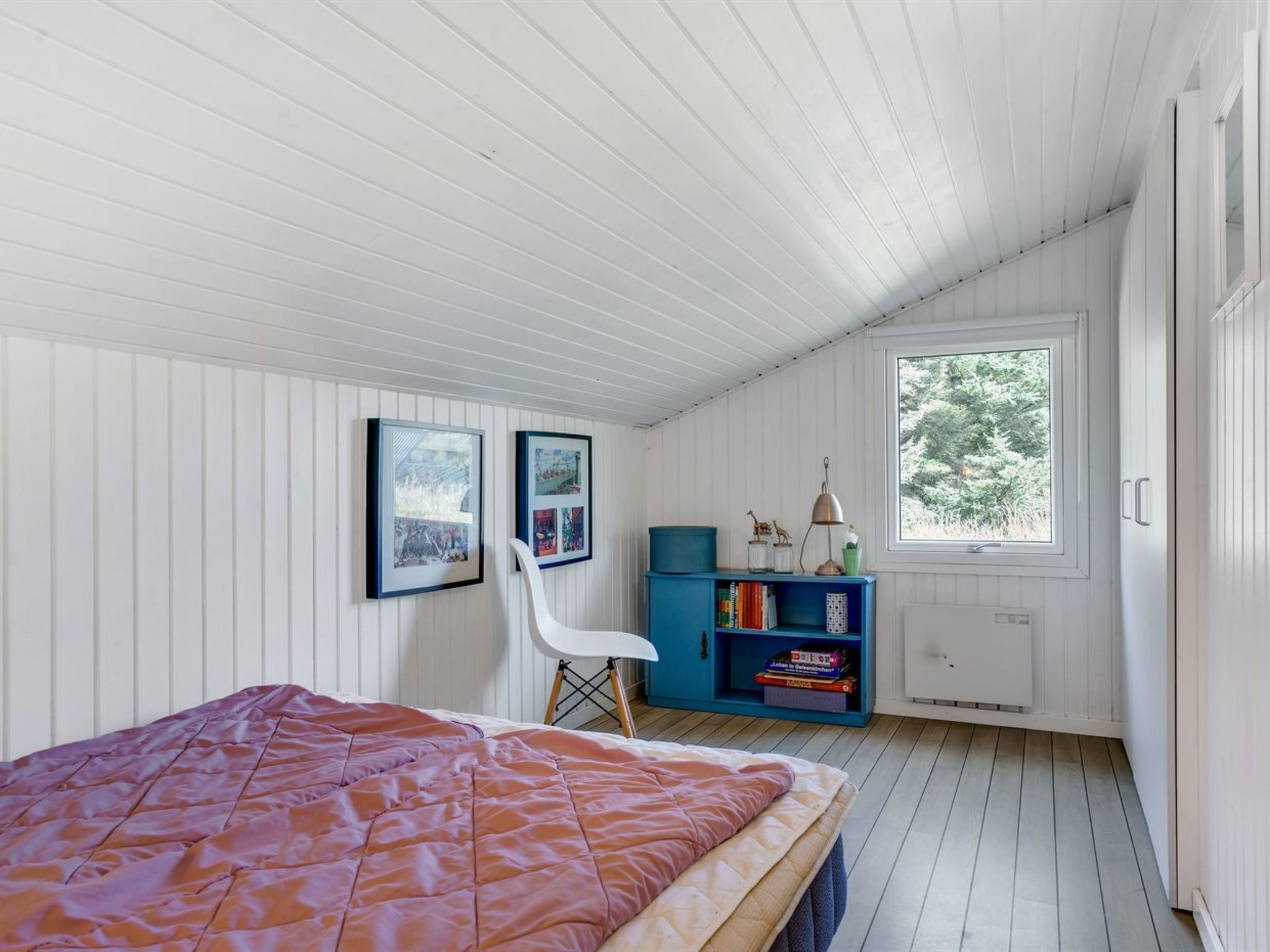 A bedroom with a bed, a blue bookshelf, and a window with a view of trees.