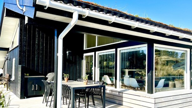 Un área de comedor al aire libre moderna con terraza de madera, sillas de metal negro y una mesa.